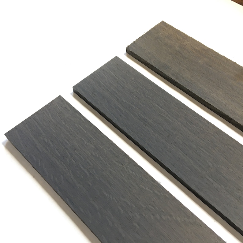 May include: Three pieces of dark gray wood, each with a different length, are arranged in a staggered pattern on a white surface.