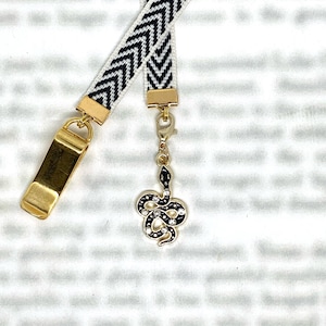 May include: Black and white chevron patterned ribbon bookmark with a gold clip and a gold snake charm with clear rhinestones.