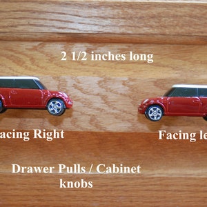 May include: Two red miniature car drawer pulls or cabinet knobs, one facing right and one facing left. The knobs are 2 1/2 inches long and 1 inch tall. "Drawer Pulls / Cabinet knobs" is written below the knobs.