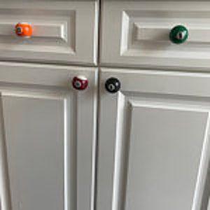 May include: Four white cabinet doors with four different colored billiard ball knobs. The knobs are orange, green, red, and black.