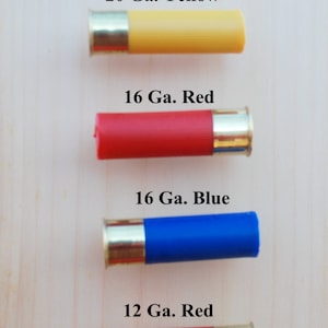 May include: Four shotgun shells in yellow, red, and blue, with brass bases. The text indicates the gauge and color: 20 Ga. Yellow, 16 Ga. Red, 16 Ga. Blue, and 12 Ga. Red. The shells are arranged vertically.