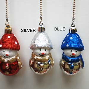 May include: Three snowman ornaments with glittery hats and scarves. The hats are red, silver, and blue with white polka dots. The scarves are gold and blue. Each snowman has a red nose and a smiling face. The word "RED", "SILVER", and "BLUE" are above each snowman.