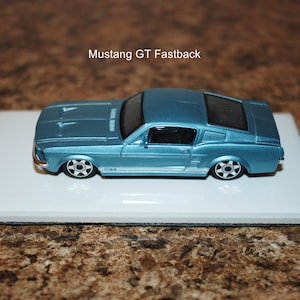 May include: A blue toy car model of a Ford Mustang GT Fastback. The car is on a white tile surface.