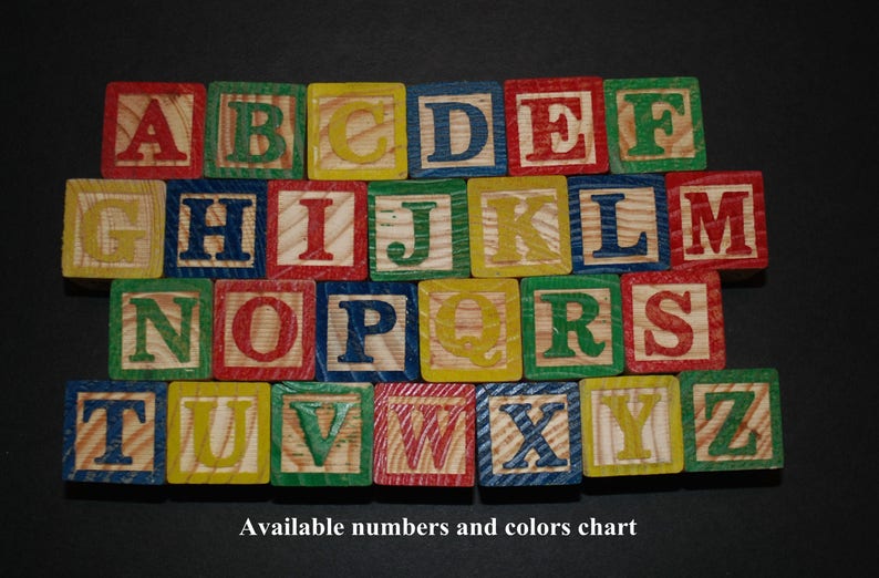 Puede incluir: Bloques de madera del alfabeto en varios colores, incluyendo rojo, azul, verde, amarillo y blanco. Cada bloque presenta una letra del alfabeto en un color contrastante.