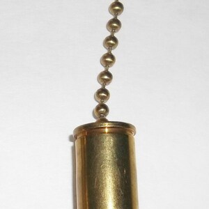 May include: A brass ceiling fan pull chain with a bullet-shaped pendant. The pendant is gold-colored with a dark gray tip, and is attached to a chain of small, round brass beads.