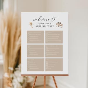 Puede incluir: Un letrero blanco sobre un caballete de cobre con el texto "welcome to OLIVIA'S NESTING PARTY". El letrero tiene un formato de lista de verificación con encabezados como "NURSERY ORGANIZATION" y "LAUNDRY". El letrero está decorado con ilustraciones temáticas de bebés.