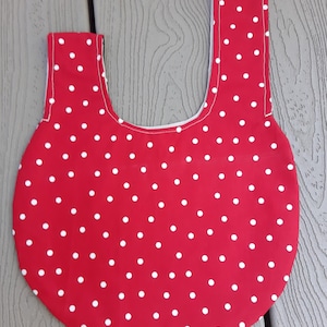 May include: Red fabric tote bag with white polka dots. The bag has a wide, rounded bottom and two straps that meet at the top.
