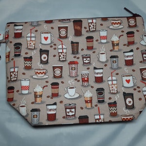 Puede incluir: Una bolsa beige con cremallera y una correa marrón. La bolsa está decorada con un patrón repetido de tazas de café, granos de café y las palabras "Espresso" y "Latte".