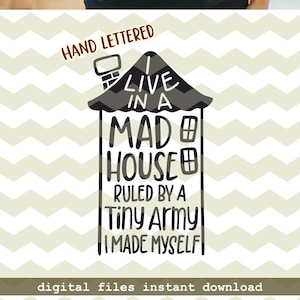 以下が含まれることがあります： 白い家のグラフィックと「I LIVE IN A MAD HOUSE RULED BY A Tiny Army I MADE MYSELF」というテキストが入った濃い青色のTシャツ。デザインは手書きです。丸い首。