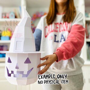 May include: A white papercraft Halloween pumpkin with a witch hat. The pumpkin has a carved face with triangular eyes and a jagged mouth. The witch hat is tall and pointed. The text "EXAMPLE ONLY NO PHYSICAL ITEM" is visible.