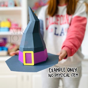 May include: A paper witch hat with a black cone and brim, a purple band, and a gold buckle. The hat is held up by a person. The text "EXAMPLE ONLY NO PHYSICAL ITEM" is printed on the bottom right.
