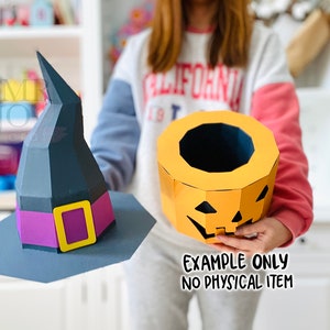 May include: A paper witch hat with a purple band and yellow buckle, and a paper jack-o'-lantern. The witch hat is dark gray and the jack-o'-lantern is orange. The text "EXAMPLE ONLY NO PHYSICAL ITEM" is visible.