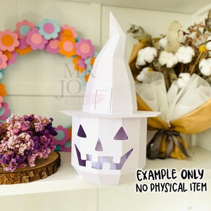 May include: A white paper jack-o'-lantern with a witch hat, a floral wreath, and dried flowers. The jack-o'-lantern has a carved face and is lit from within. The text "EXAMPLE ONLY NO PHYSICAL ITEM" is visible.