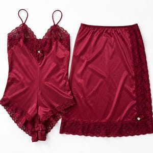 May include: A deep burgundy lingerie set consisting of a camisole and a matching skirt. The camisole features thin spaghetti straps, a V-neckline with lace trim, and a small decorative bow. The skirt has a side lace panel and a matching bow detail.