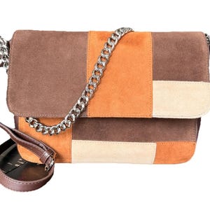 May include: A patchwork suede shoulder bag in shades of brown, orange, and cream. The bag features a silver chain strap and a brown leather adjustable shoulder strap. The flap closure is secured with a magnetic snap.