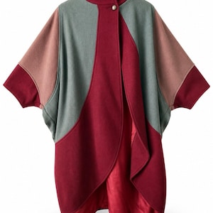 May include: A color-blocked cape featuring a high collar with a single button closure. The garment is constructed from panels of deep burgundy, muted sage green, and dusty rose fabric, with a smooth, solid burgundy lining visible at the front.