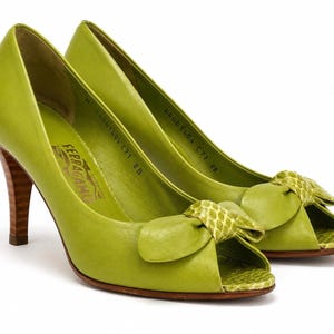 May include: A pair of lime green peep-toe high heels with bow accents. The heels have a wooden-look finish. The shoes are leather and feature the brand name "Ferragamo".