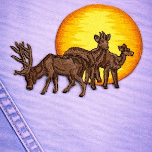 May include: Embroidered patch featuring three brown deer in front of a yellow sun. The patch is sewn onto a light blue denim fabric. The deer have detailed antlers and are in a naturalistic style.