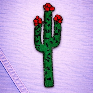 May include: Embroidered green cactus patch with red flower accents and black detailing. The patch is on a light blue fabric background. The cactus design is a fun, decorative element for clothing or accessories.