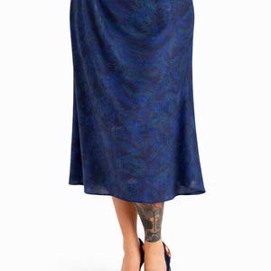 May include: A knee-length blue skirt with a dark blue and green leaf pattern. The skirt is paired with dark blue high heels with floral embroidery. The skirt has a flowing, A-line shape.