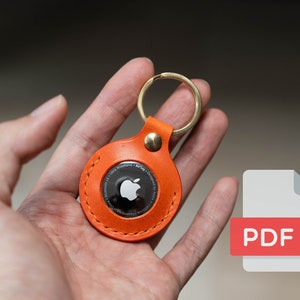 May include: Orange leather keychain with a stitched edge and a round metal disc featuring the Apple logo.