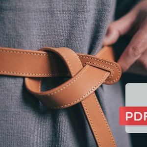 以下が含まれることがあります： 人の腰に結ばれた茶色の革製のベルト。ベルトはステッチが施された縁取りがあり、柔らかくしなやかな革で作られています。