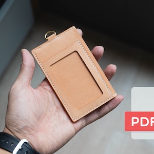 May include: A brown leather ID card holder with a stitched border and a clear plastic window for displaying an ID card. The holder has a gold metal ring for attaching a lanyard.  PDF