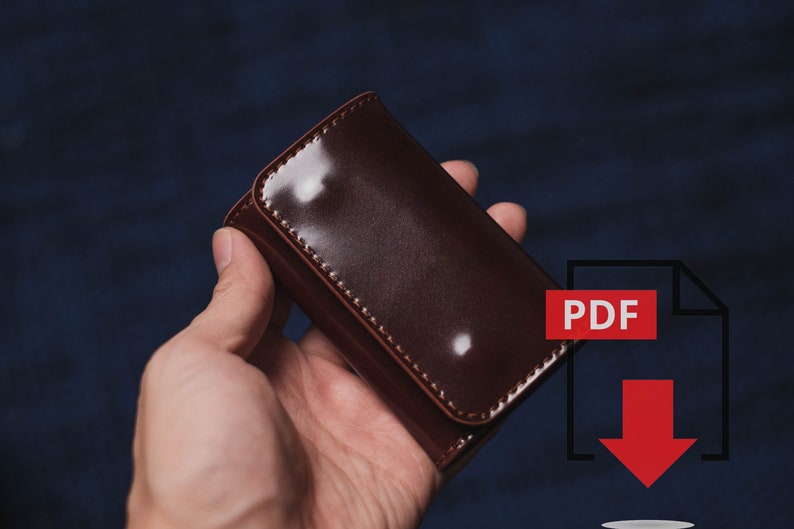 Pu&ograve; includere: Un portachiavi in pelle marrone scuro lucido con chiusura a scatto. Il portachiavi rettangolare &egrave; tenuto in mano su uno sfondo blu scuro. Un'icona PDF rossa con una freccia rivolta verso il basso si trova nell'angolo in basso a destra.