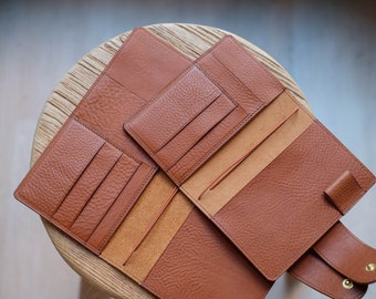 May include: A brown leather wallet with multiple card slots and a flap closure. The wallet is open to reveal a tan interior with additional slots and a pen loop.