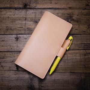 May include: A light brown leather notebook with a yellow pen tucked into the pocket.