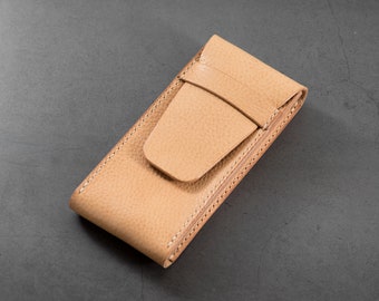 May include: A tan leather case with a flap closure. The case is designed to hold a small object, such as a pen or a phone.