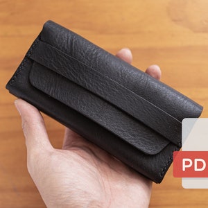 May include: A black leather wallet with a flap closure. The wallet is held in a hand.