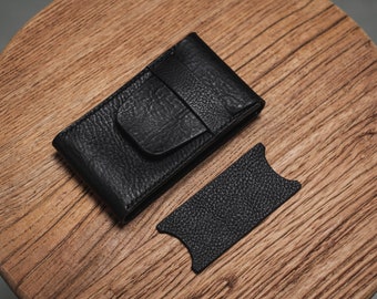 May include: A black textured leather card holder with a flap closure and a separate rectangular black leather piece featuring curved cutouts on the short sides, both displaying a consistent pebbled grain finish and visible stitching details.