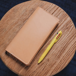 May include: A light brown leather notebook with a yellow pen on a wooden surface.