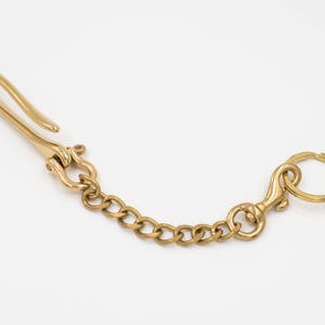 Könnte beinhalten: Ein goldfarbener Schlüsselanhänger mit einem Haken an einem Ende und einem Ring am anderen Ende. Die Kette besteht aus einer Reihe von miteinander verbundenen Metallschlaufen.