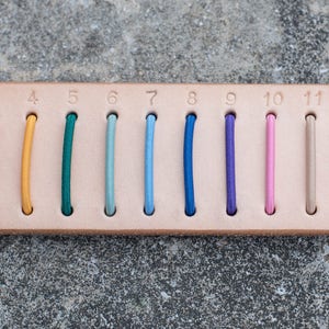 May include: A leather swatch with 14 different coloured leather strips numbered 1 through 14. The word "COLORS" is printed on the left side of the swatch.