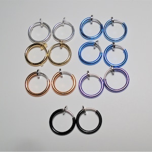 May include: A set of ten non-pierced earrings in various colours, including silver, gold, blue, and purple. The earrings are all round and have a simple design.