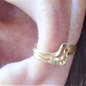 May include: Gold ear cuff with a wavy design. The cuff is made of three thin bands of metal.