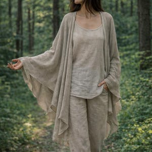 Könnte beinhalten: Ein neutralfarbenes Leinen-Ensemble, bestehend aus einem Tanktop, einer Hose und einer langen, fließenden Strickjacke. Das Outfit hat einen hellbeigen Farbton und erzeugt einen weichen, natürlichen Look. Die Kleidung wirkt leicht und bequem, geeignet für Freizeitkleidung.