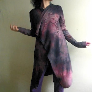 Peut inclure: Longue veste ouverte sur le devant, dans des tons de violet et de noir, avec un motif unique sur la partie supérieure. La veste a des manches longues et un design asymétrique. Le modèle porte un pantalon violet.