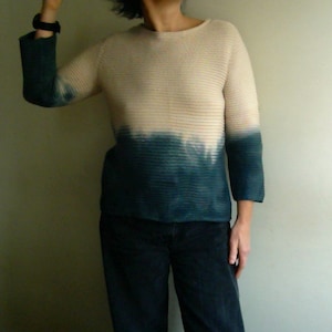 May include: A long-sleeved, knitted sweater with a tie-dye design. The sweater is white at the top and fades to a dark blue at the bottom.