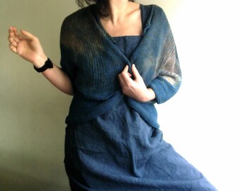 May include: A blue knitted cardigan with a long, flowing skirt. The cardigan has a loose, open weave and a slightly textured surface. The skirt is made of a soft, drapey fabric.