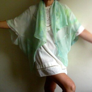 Peut inclure: Une femme portant une robe blanche avec une écharpe en mousseline verte et bleue drapé sur ses épaules. L'écharpe a un motif tie-dye.
