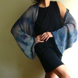 Peut inclure: Un châle en tricot bleu et gris avec un motif tie-dye. Le châle est drapé sur les épaules et les bras d'une personne.