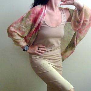 Peut inclure: Une robe débardeur beige sans manches associée à un châle léger et semi-transparent présentant un motif de style aquarelle dans des tons de rose, de vert et de beige. Le châle se drape sur les épaules, complétant la teinte neutre de la robe.