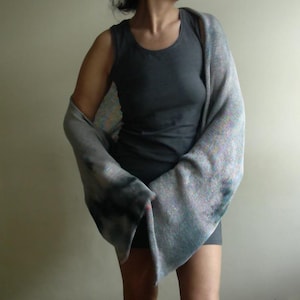 Peut inclure: Une robe grise et un châle assorti. Le châle est drapé sur les épaules et les bras. Le châle a un effet tie-dye avec des teintes grises et bleues plus foncées. La robe est de conception simple et sans manches.