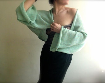 May include: A light green knitted shrug with long sleeves and a draped neckline. The shrug is made of a soft, lightweight fabric and is perfect for layering.
