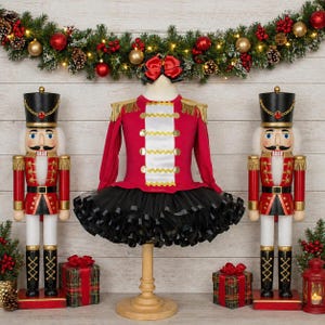 May include: A red and black Nutcracker-themed outfit with gold accents, displayed on a wooden stand. The outfit includes a red top with gold trim and a black tutu skirt. Two Nutcracker figures flank the outfit, with festive decorations in the background.