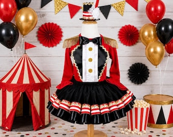 May include: A ringmaster costume featuring a red jacket with gold fringe epaulets, a white vest front with three gold buttons, and a black bowtie. The skirt is a black tutu with red and white striped ribbon trim. A matching mini top hat is included.