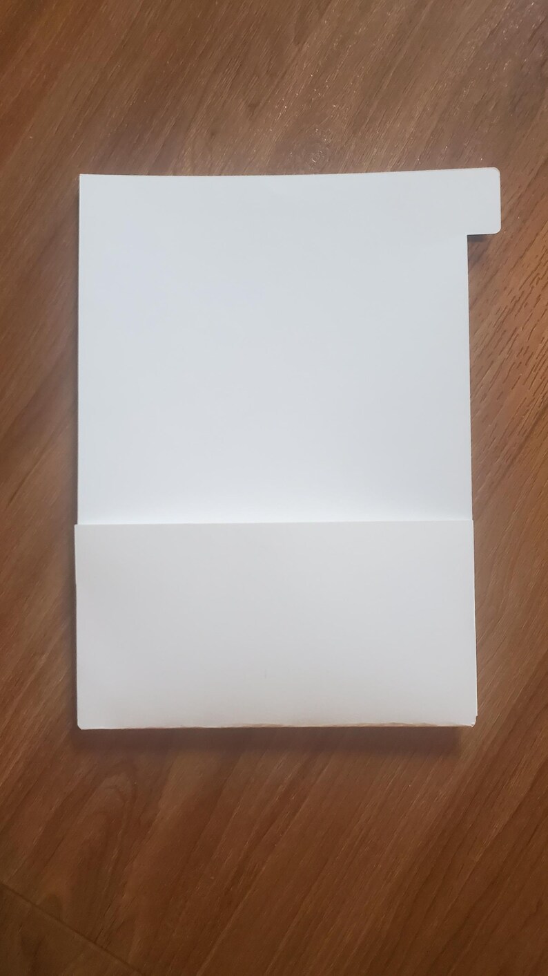 Puede incluir: Una carpeta de archivos blanca con una pesta&ntilde;a en la esquina superior derecha. La carpeta est&aacute; doblada por la mitad para crear un bolsillo.